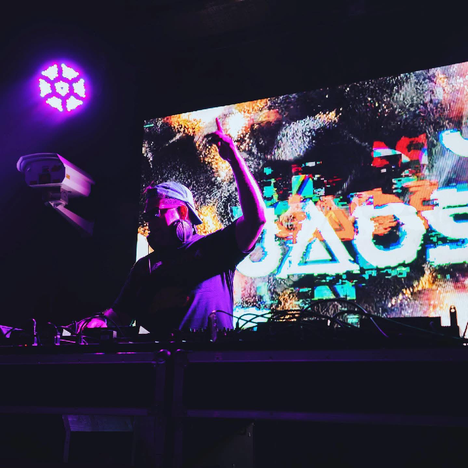 Jose Ortega performing as JAOS with one arm raised under purple stage lights.